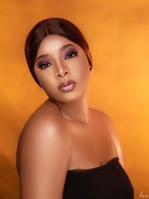 Portrait Of A Woman With Sleek Dark Hair Posing Against A Warm Orange Toned Studio Background.